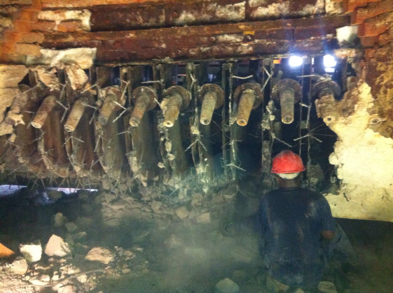Cross Refractory crew member beside refractory burner blocks in a furnace wall being stripped for relining